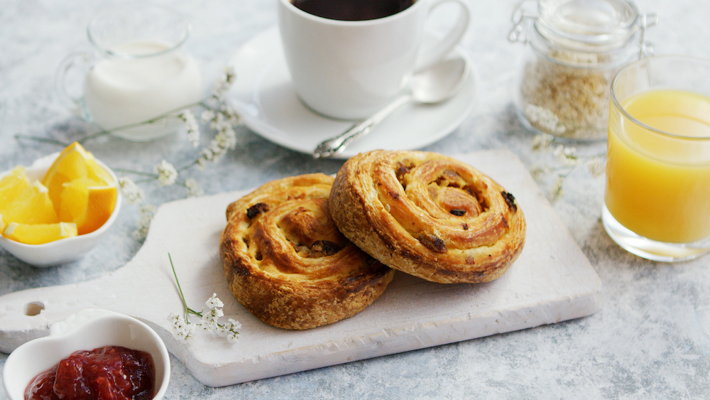 Served delicious breakfast meal with baked buns on wooden board on marble table with coffee and juice and jam